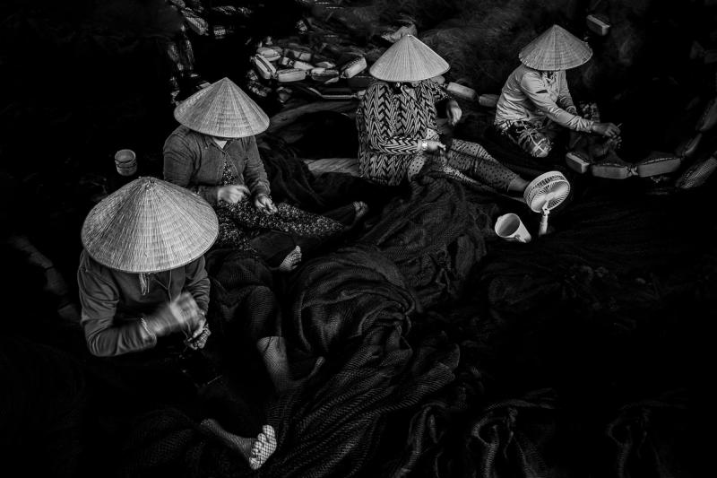 People in conical hats mending fishing nets in a black-and-white photograph
