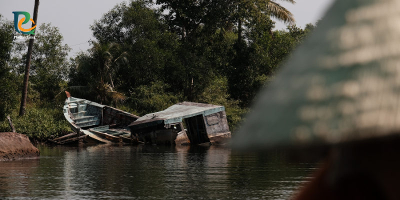 An old wooden fishing boat beside a wooded Cua Can riverbank