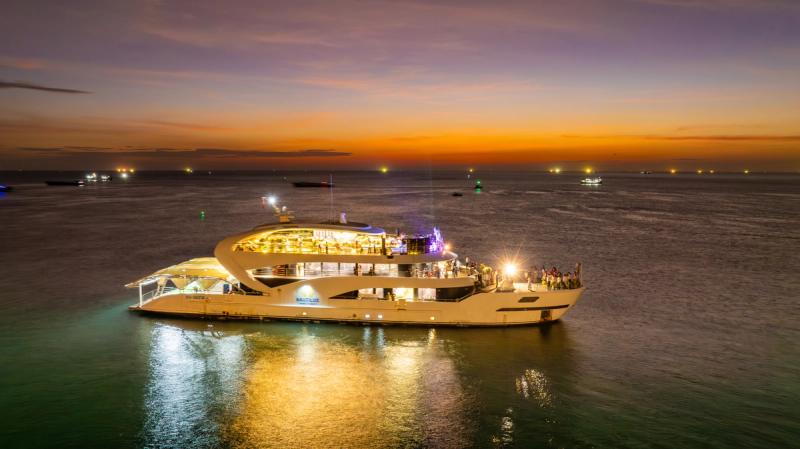 An illuminated yacht on the sea beneath an orange dusk sky