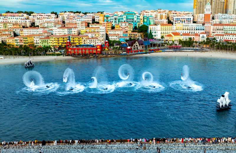 A line of watercraft and jets of spray performing off a colourful waterfront