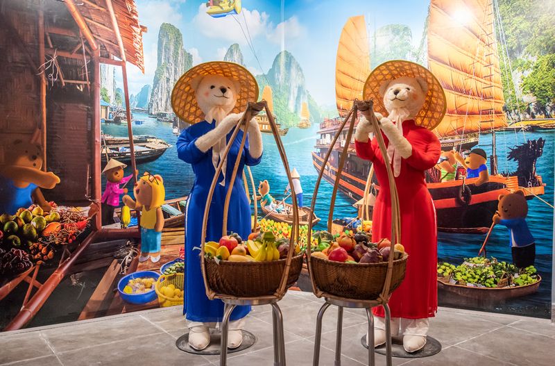 Gấu bông mặc trang phục người bán hàng cầm giỏ trong mô hình chợ ở bảo tàng