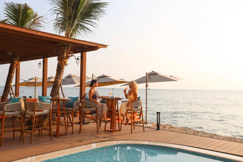 Two guests at a seaside terrace table beside a swimming pool