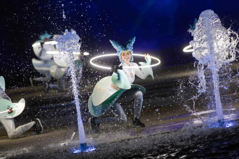 A costumed performer with a luminous hoop between fountains