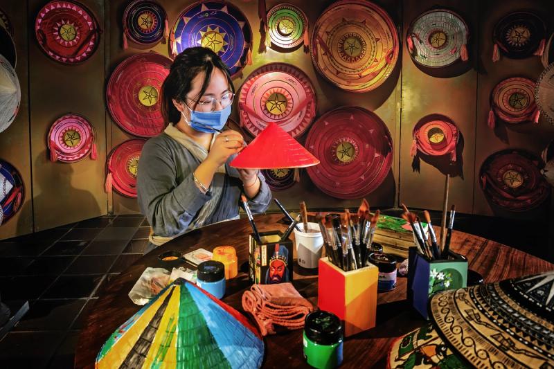 A craftsperson painting a red conical hat at a worktable