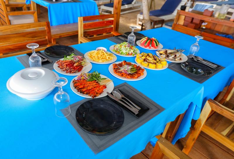 Several prepared dishes arranged on a blue-covered dining table with wooden chairs