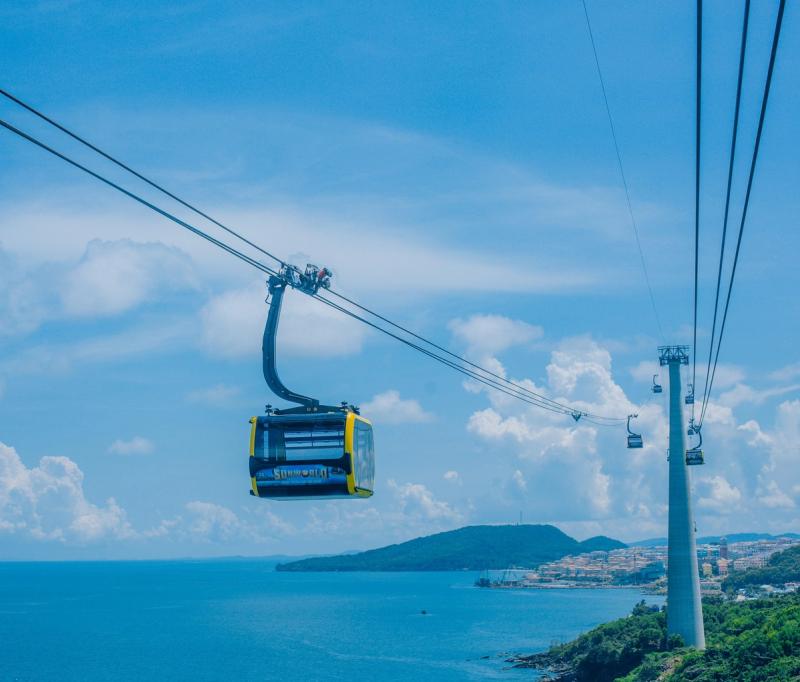 A yellow cable-car cabin beside a tower over a coastal hillside