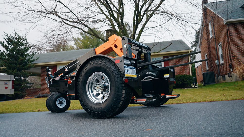 An Equipter Tow-A-Lift parked on a residential driveway with its oversized flotation tire and forks in the foreground.