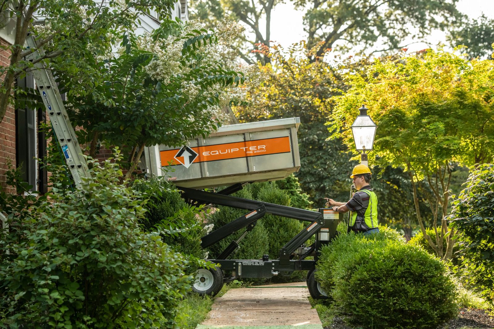 Equipter 2500 raised on a narrow garden walkway between shrubs during a roof tear-off