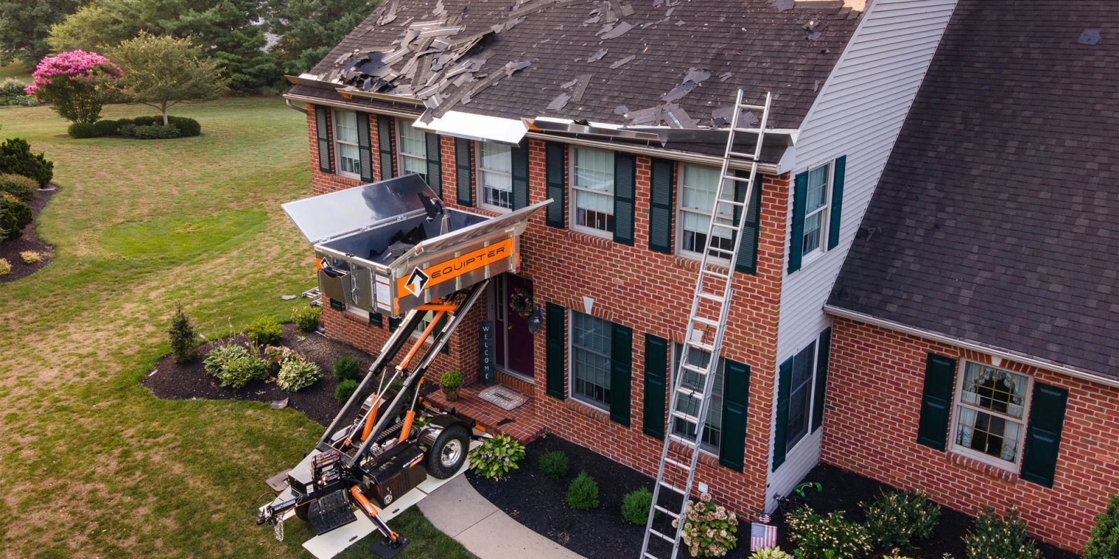 Equipter 4000 with its container raised to the roof edge of a two-story brick home