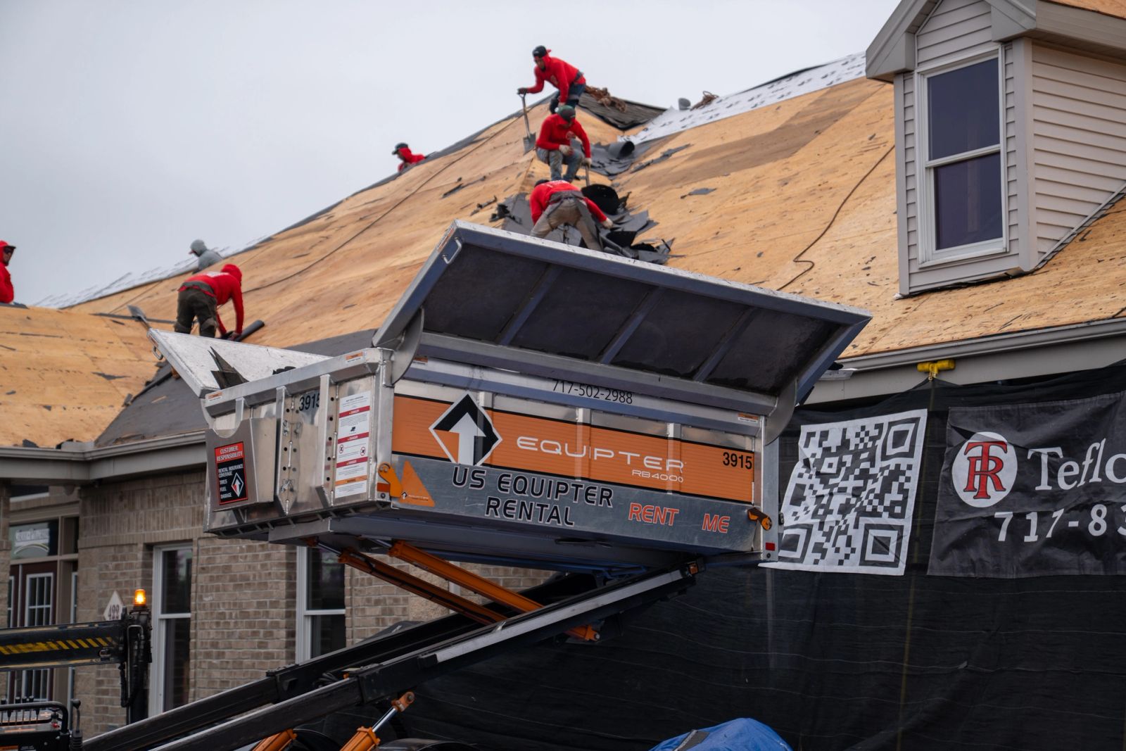 Roofing crew tearing off shingles into an Equipter 4000 raised at the eave