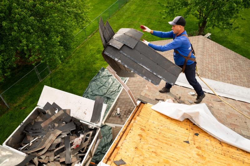 A roofer tossing torn-off shingles directly into the raised Equipter 4000 container at the roof edge.
