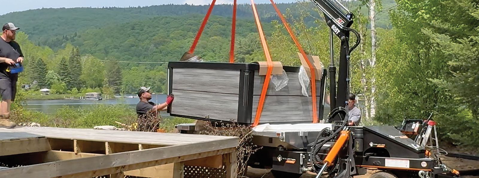 Equipter 5400 crane lifting a hot tub on straps onto a new deck while two workers guide it into place