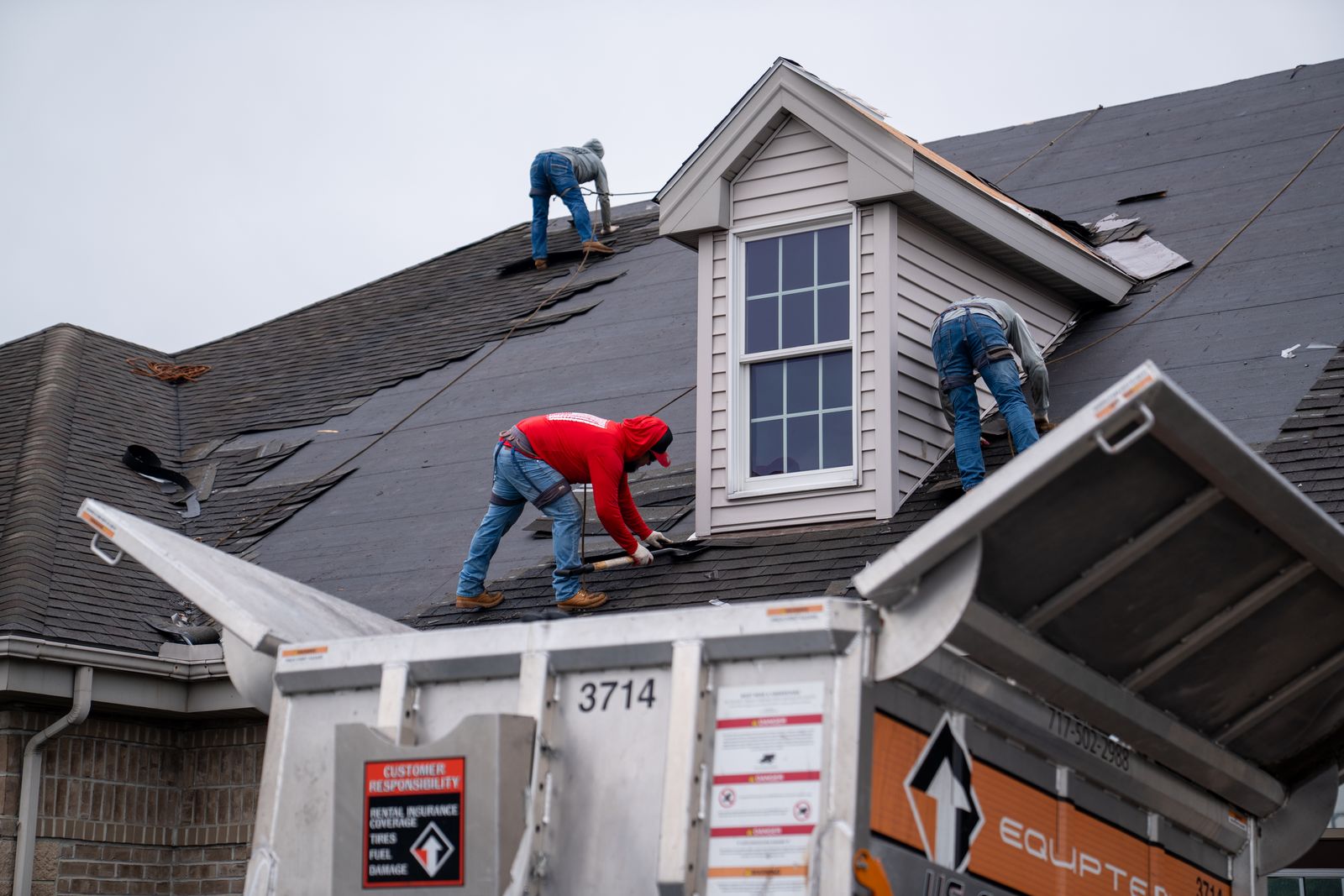 Roofers stripping shingles above an Equipter 4000 raised at the roof edge
