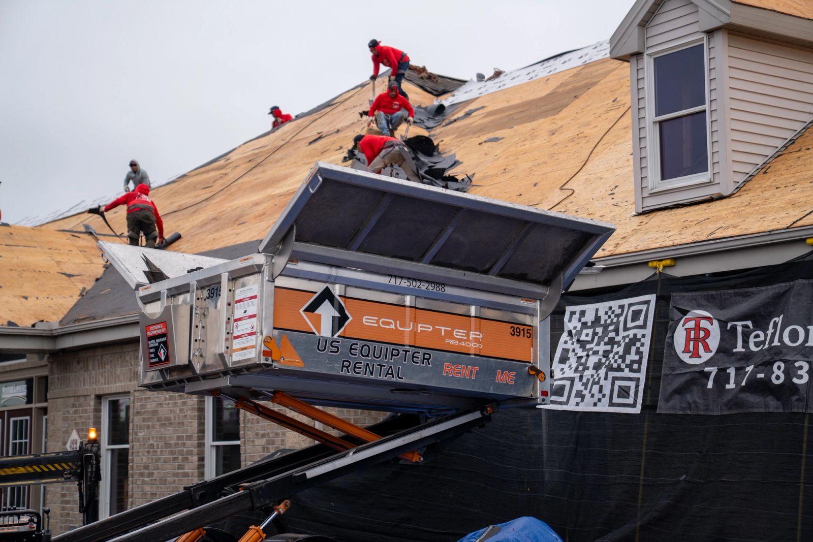 Roofing crew tearing off shingles into an Equipter 4000 raised at the eave