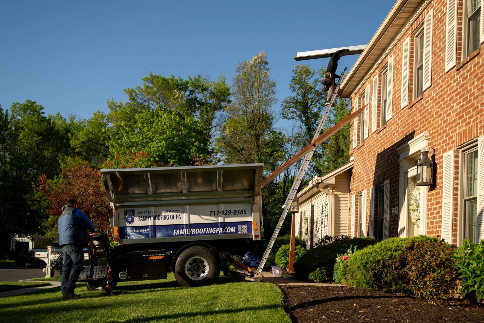 An Equipter 4000 raised to the second story of a brick colonial home in early morning light during a residential re-roof.