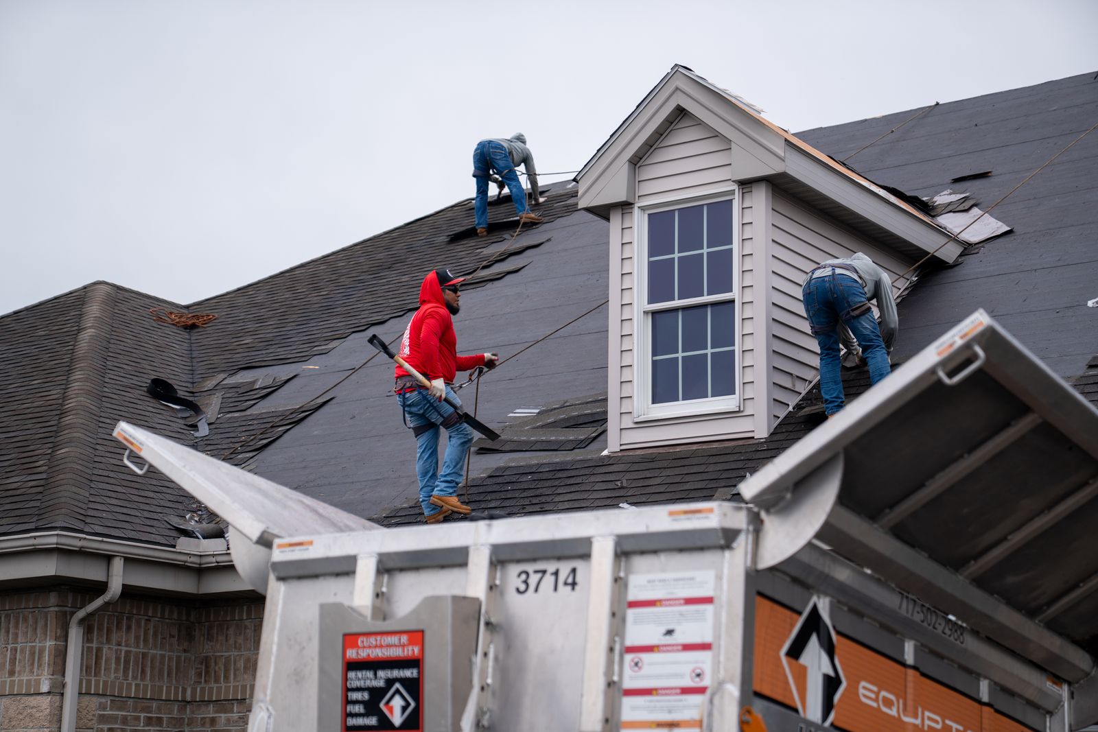 Roofers using tear-off shovels on a steep roof above a raised Equipter 4000