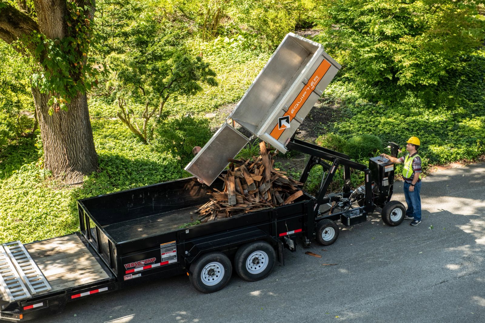 Equipter 2500 lifting and dumping roofing debris into a dump trailer at the curb