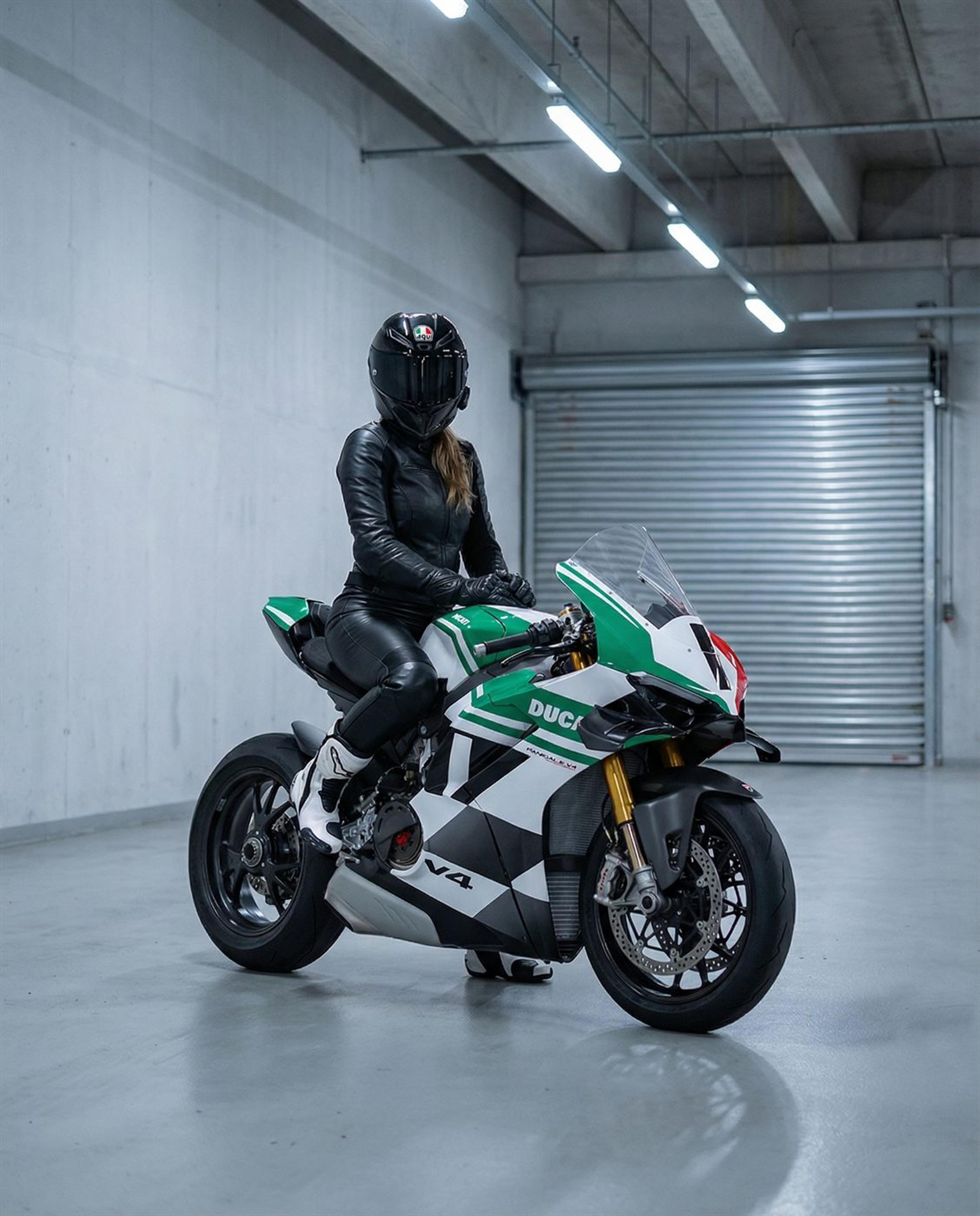 Rider in full leathers astride a green and white superbike inside a bare concrete warehouse