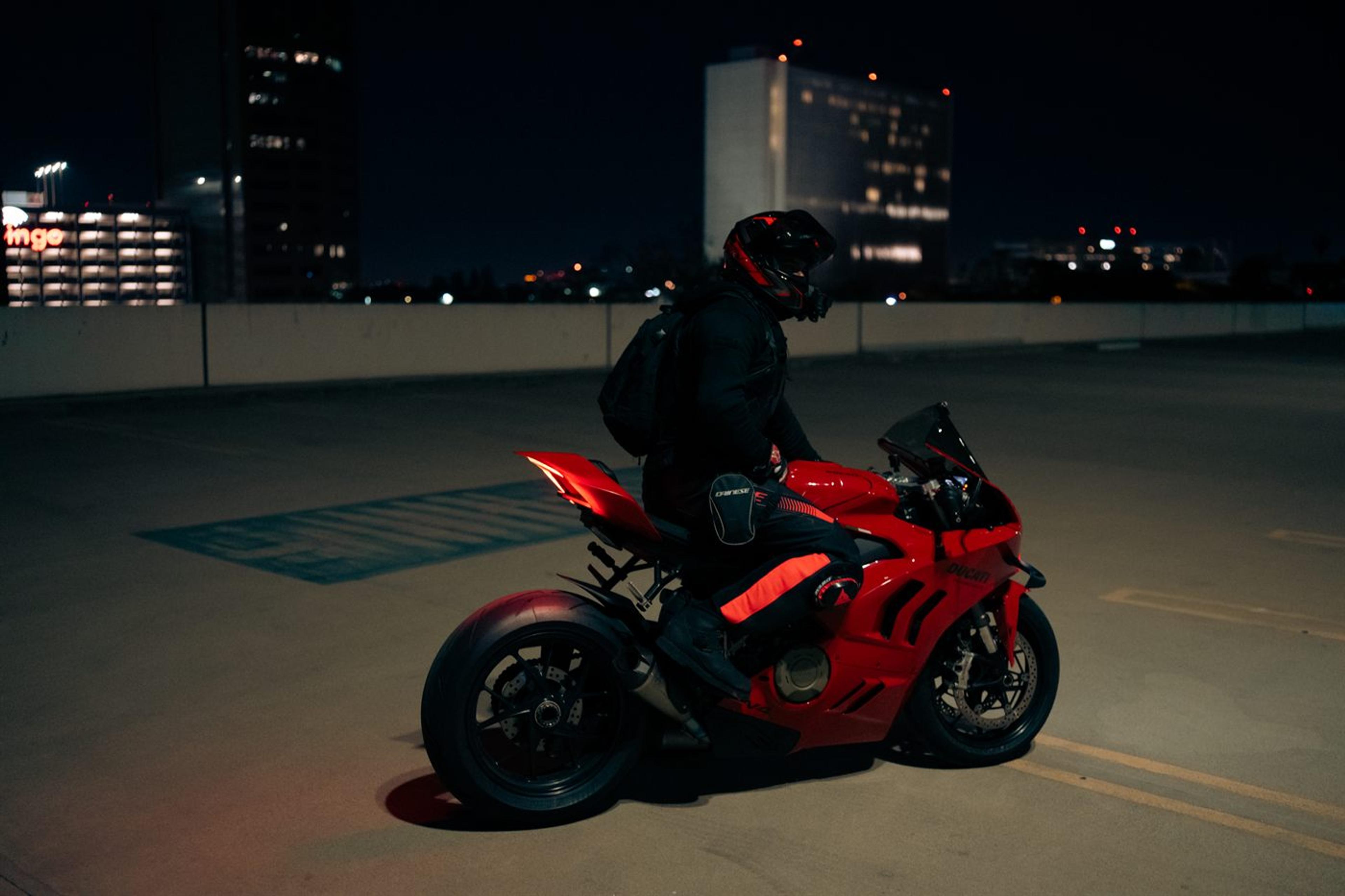 Rider on a red Ducati on a rooftop deck at night with the Los Angeles skyline behind