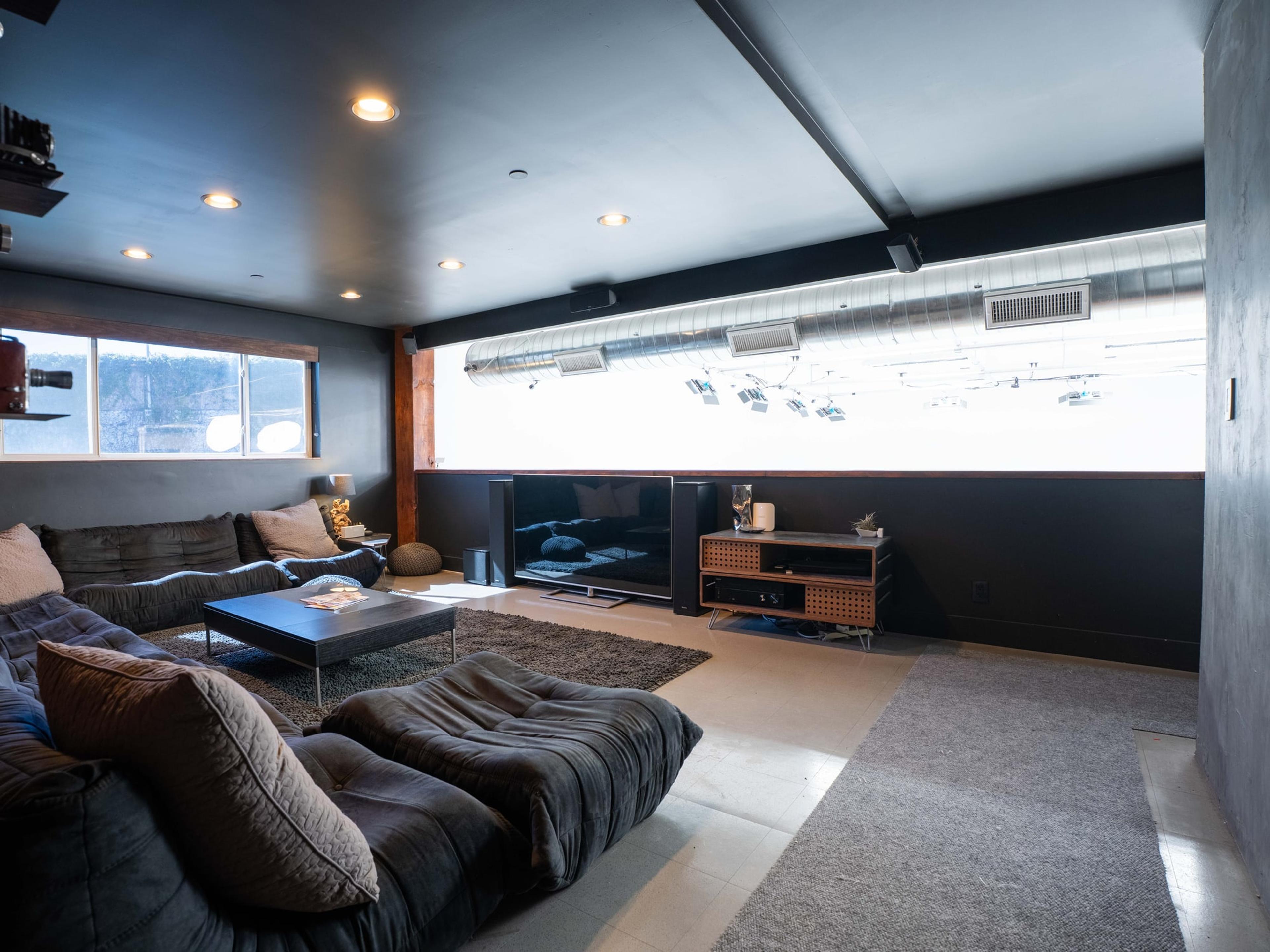 Client lounge with a timber camera wall, deep sectional and a window to the hills