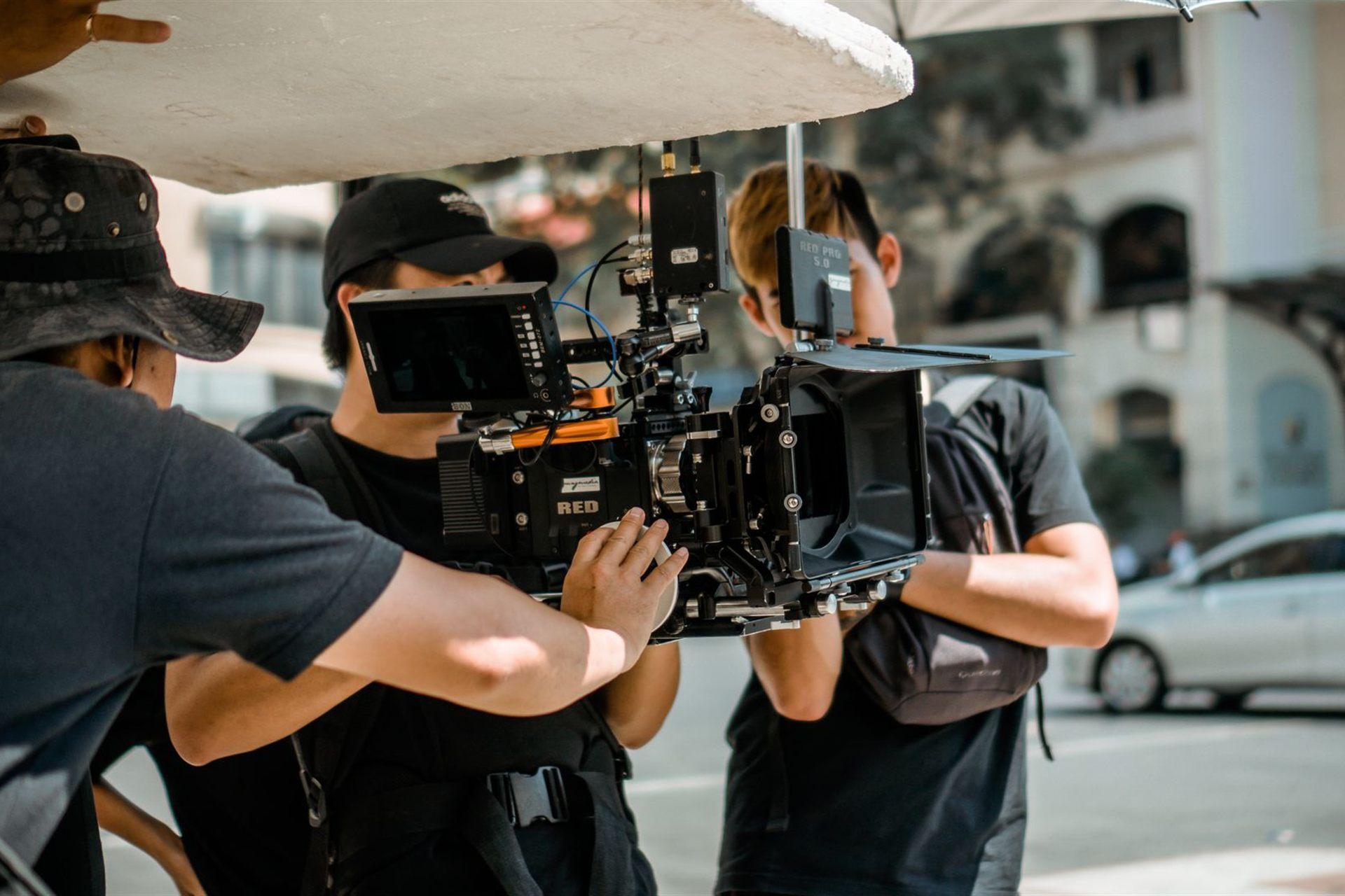 Camera crew operating a RED cinema camera on a city street under a bounce board