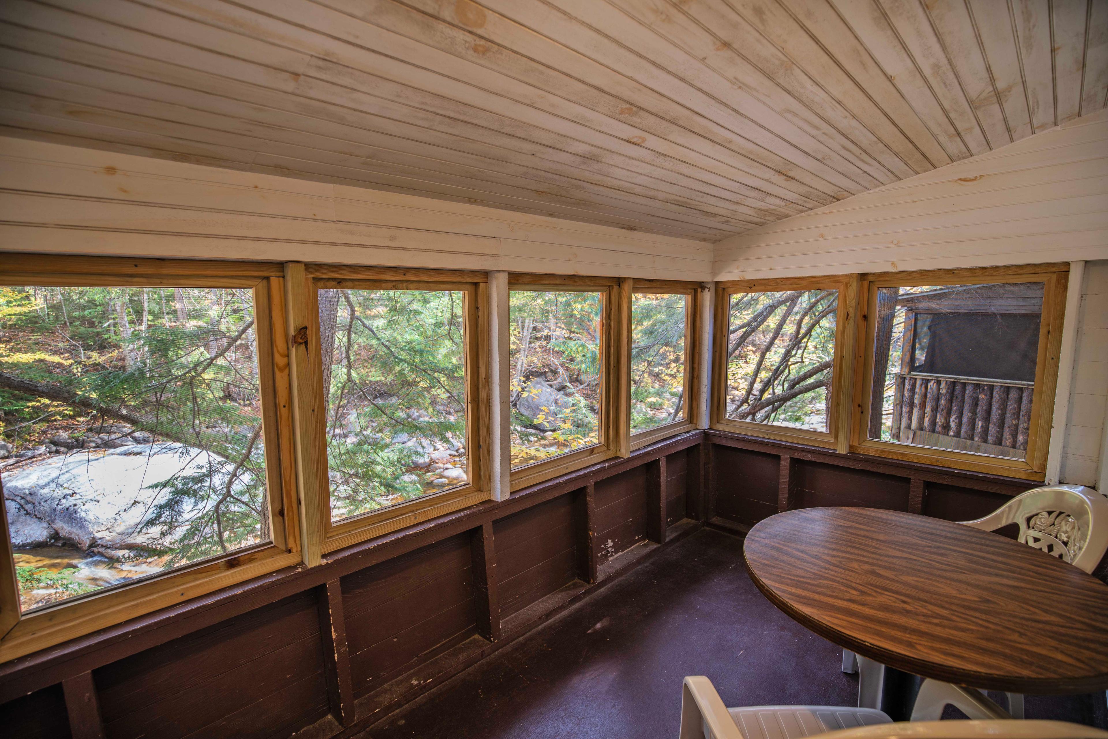 Screened-in porch with stunning views of the Pemigewasset River at Beaver Pond. #NatureLovers #CabinGetaway #ScenicViews #YearRoundComfort