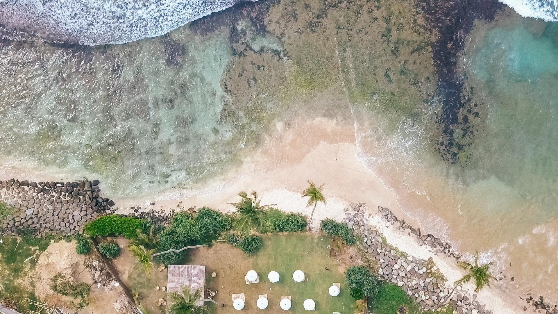 Aerial view of tropical beach resort with pool, umbrellas, and white sand cove