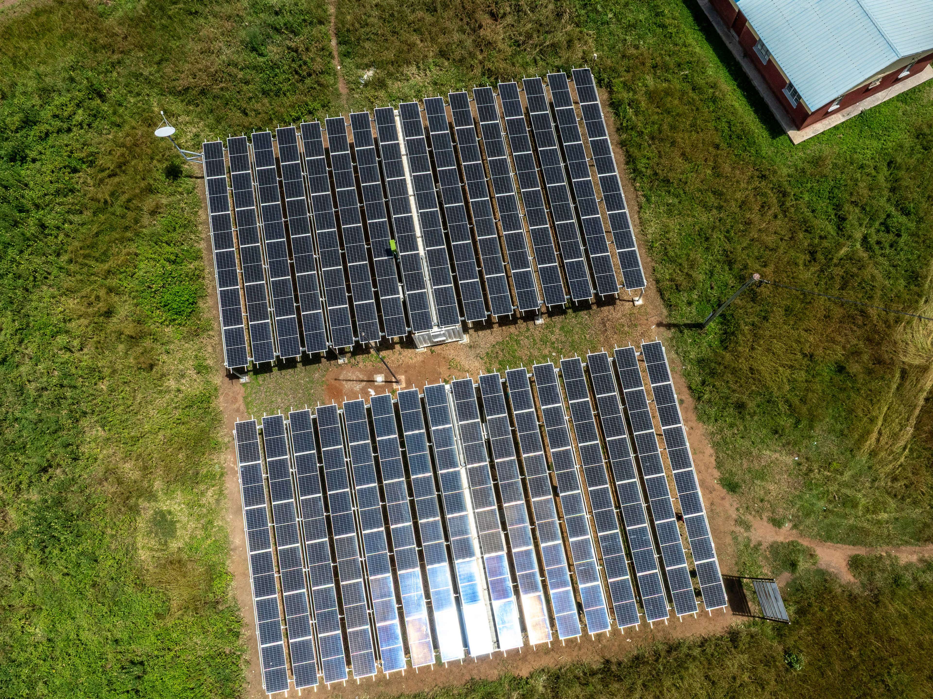 Aerial view of two large solar panel arrays in a grassy field next to a building.