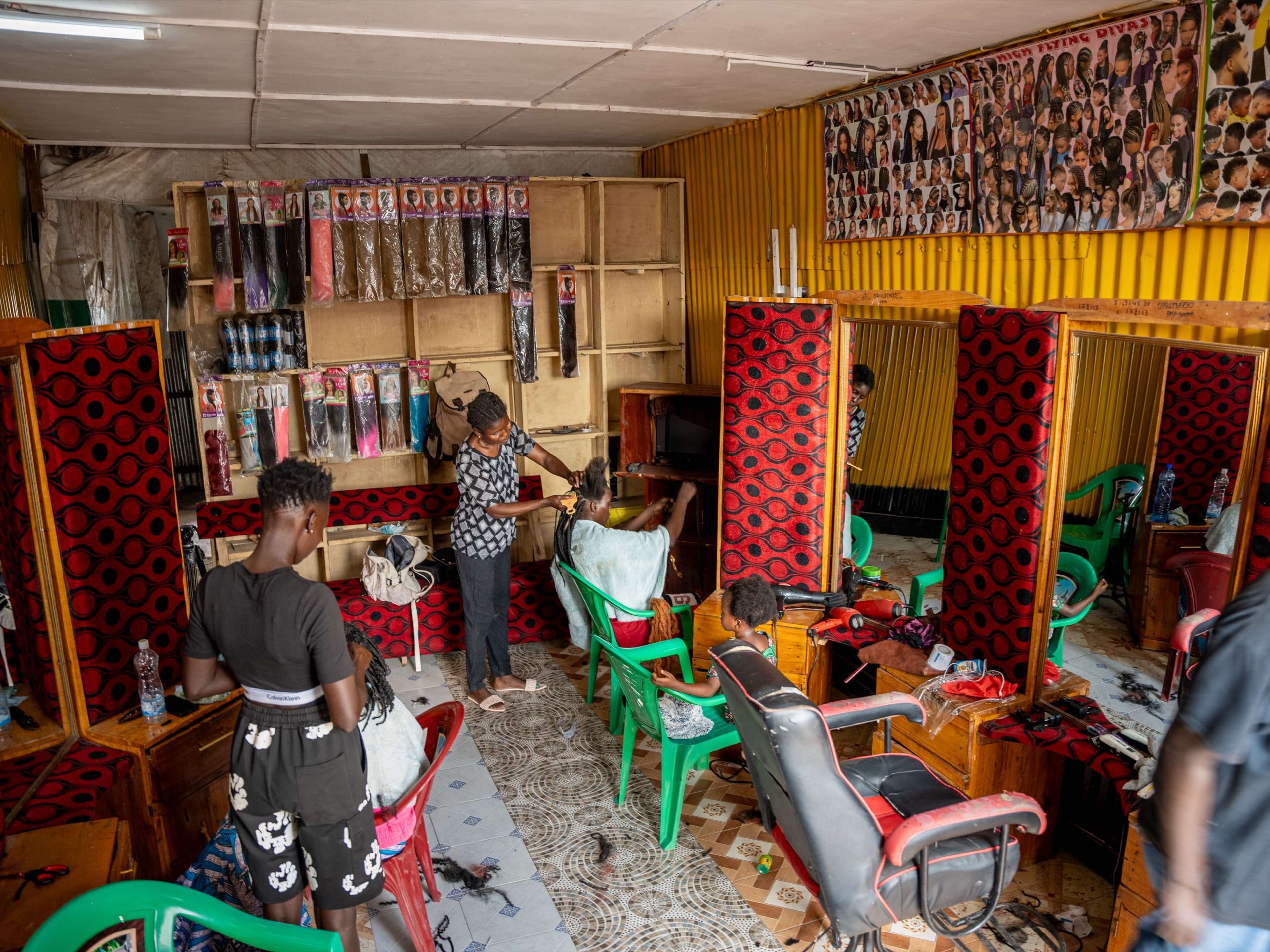 A vibrant hair salon with stylists working on clients, surrounded by mirrors, hair extensions, and a hairstyle poster.