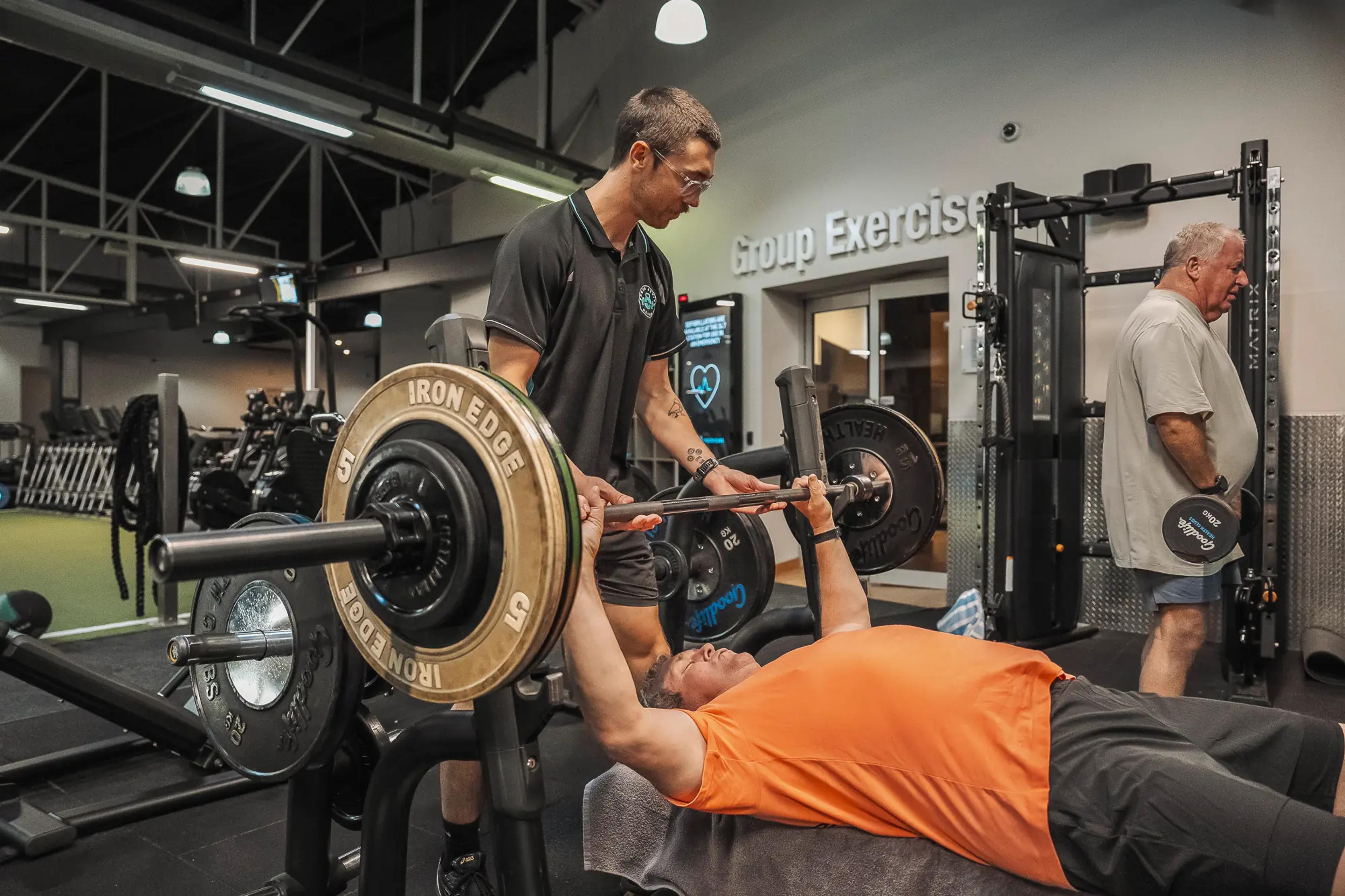Trainer spotting client during bench press workout, focused and supportive.