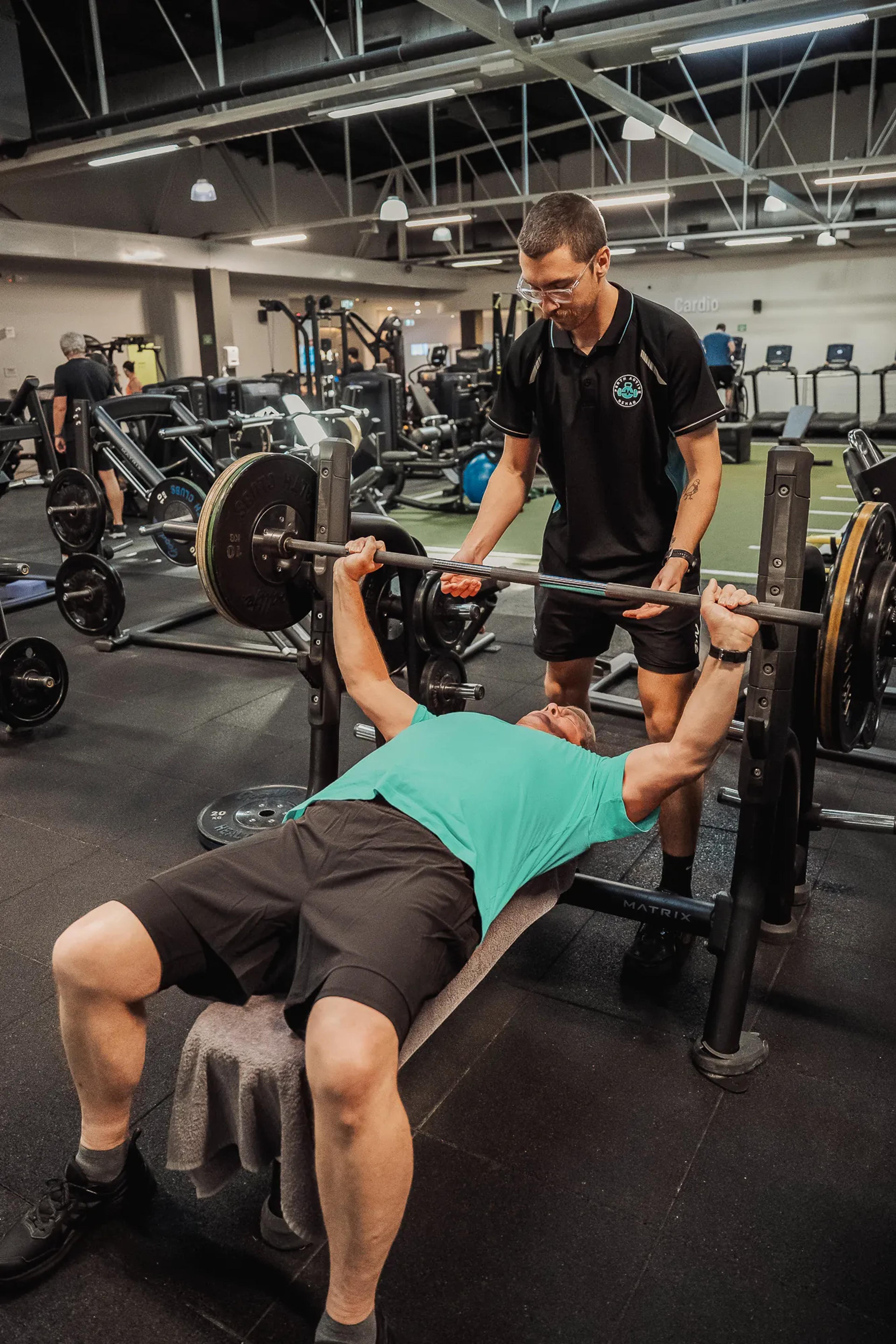 Motivated man bench pressing with focused support from his exercise physiologist in a modern gym