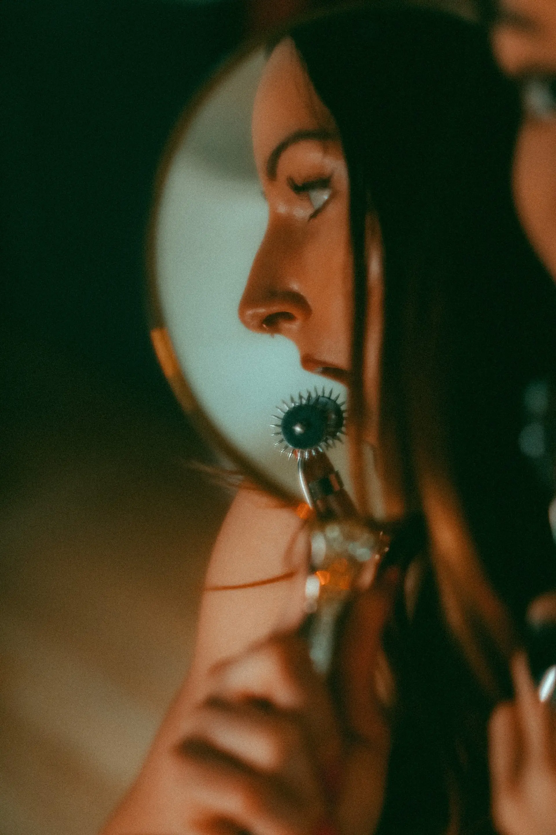 Mistress Hex holding a warten wheel in her mouth. Her face is reflected in a mirror.