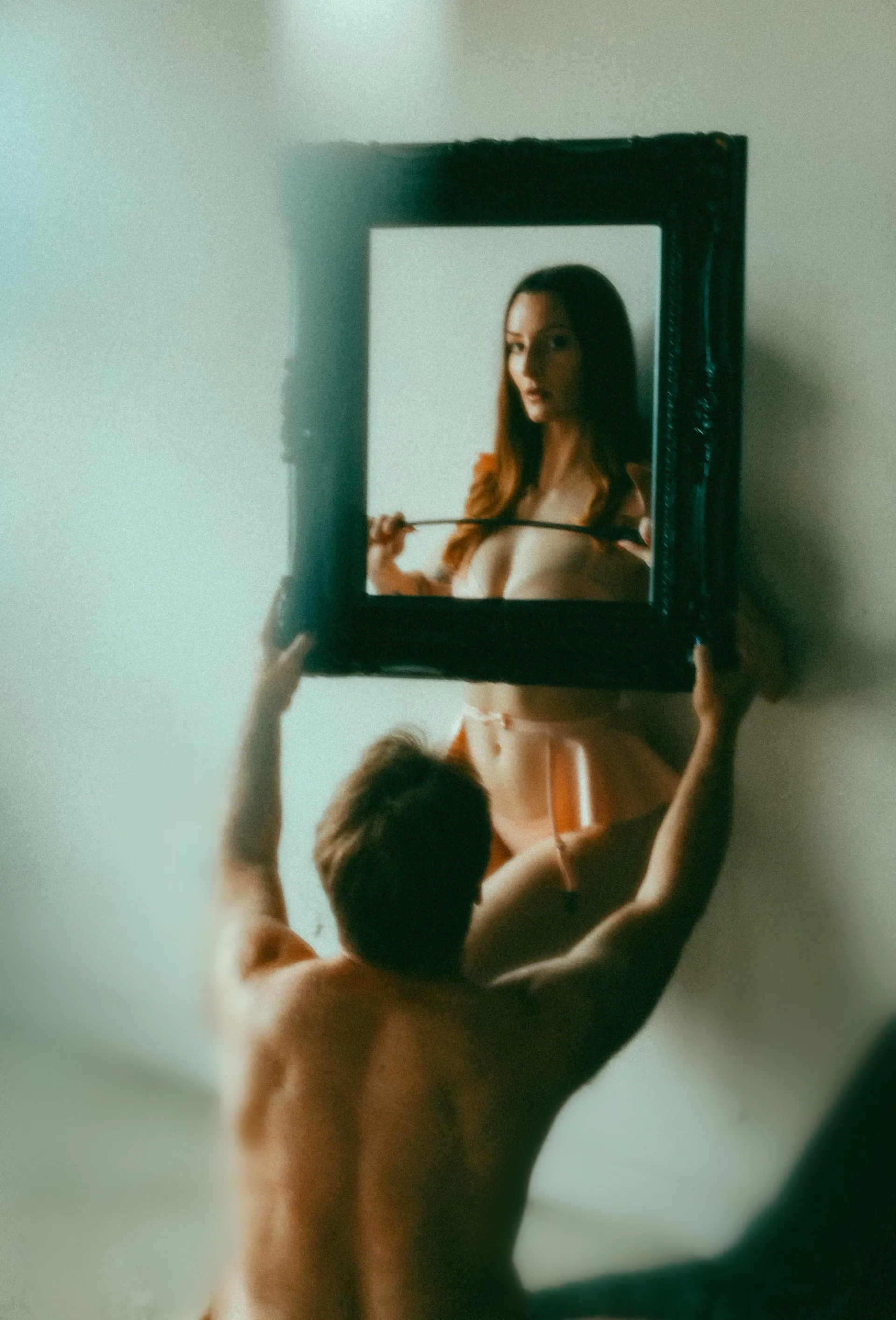 A submissive holding up a painting frame, with Jennifer Hex as the portrait.