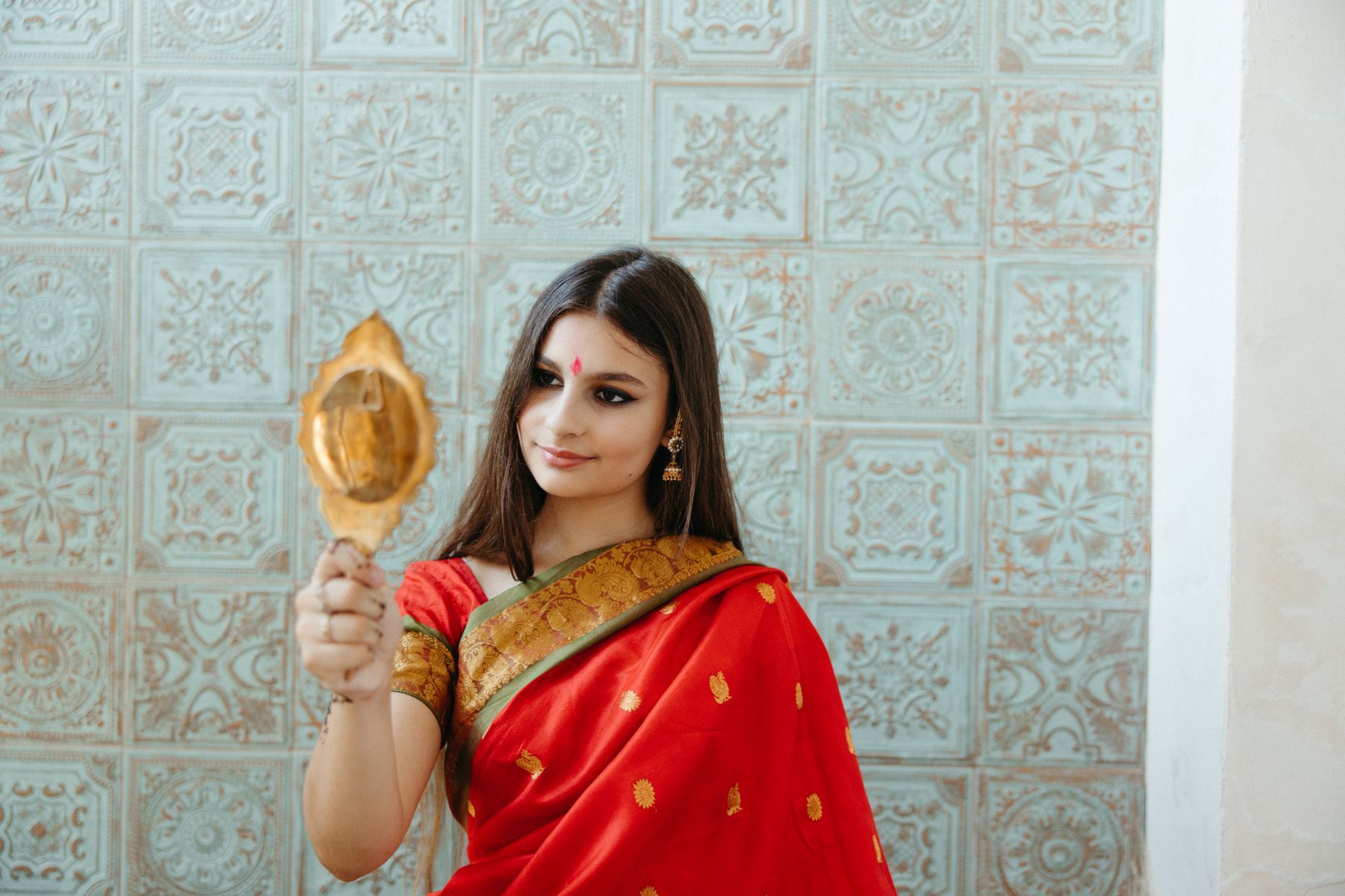Woman in a red sari holding a hand mirror