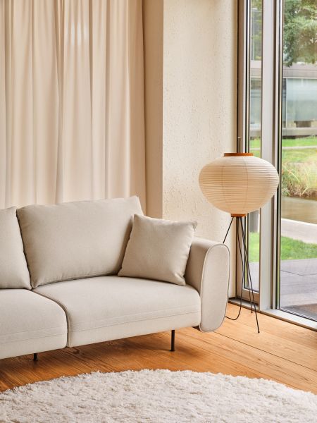 Svetlý dizajnový gauč Lotus s vankúšom v modernom interiéri pri veľkom okne a stojacej lampe