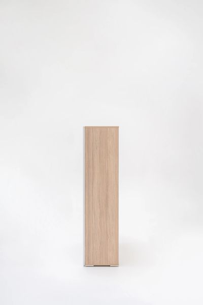 Bočný pohľad na úzku drevenú skriňu Mito so sklenenými dverami v minimalistickom bielom priestore