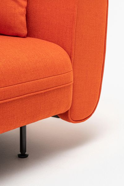 Detail oranžovej sedačky Lotus s oblým podrúčkou a čiernou kovovou nohou na svetlej podlahe