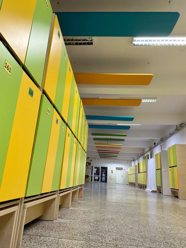 Školská chodba v Trnave s farebnými stropnými akustickými panelmi a radom žltých a zelených skriniek