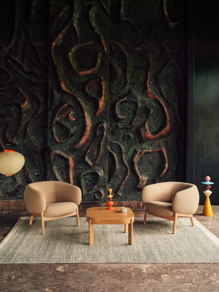 Alt: Dve béžové kreslá Grand Grace s drevenými nohami pri nízkom stolíku na koberci pred umeleckou stenou.
Titulok: Elegantné komfortné kreslá Grand Grace s prirodzeným dreveným detailom, doplnené nízkym stolíkom a dekoráciami v modernom interiéri.