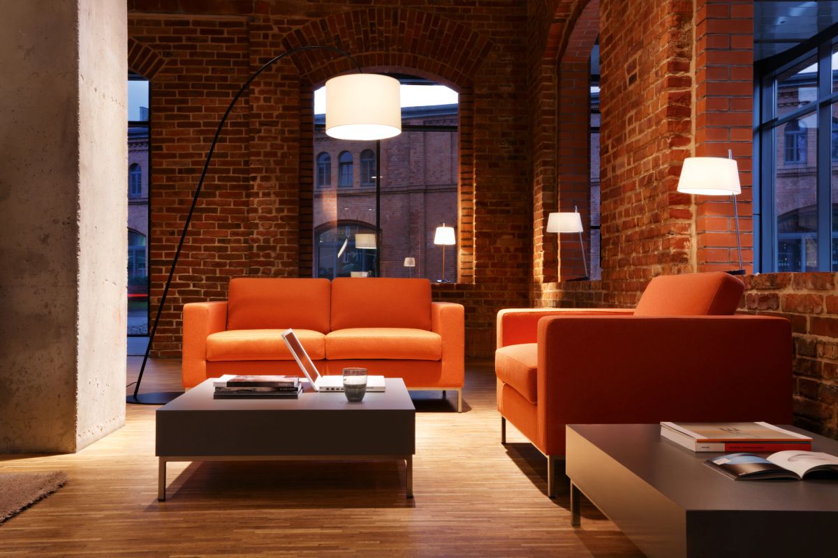 Oranžová sedačka MyTurn Sofa v industriálnom reprezentatívnom priestore s tehlovými stenami a dizajnovým osvetlením