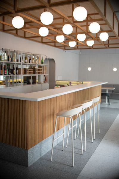 Moderný bar s dreveným pultom, bielymi vysokými stoličkami Team a guľovými závesnými svetlami