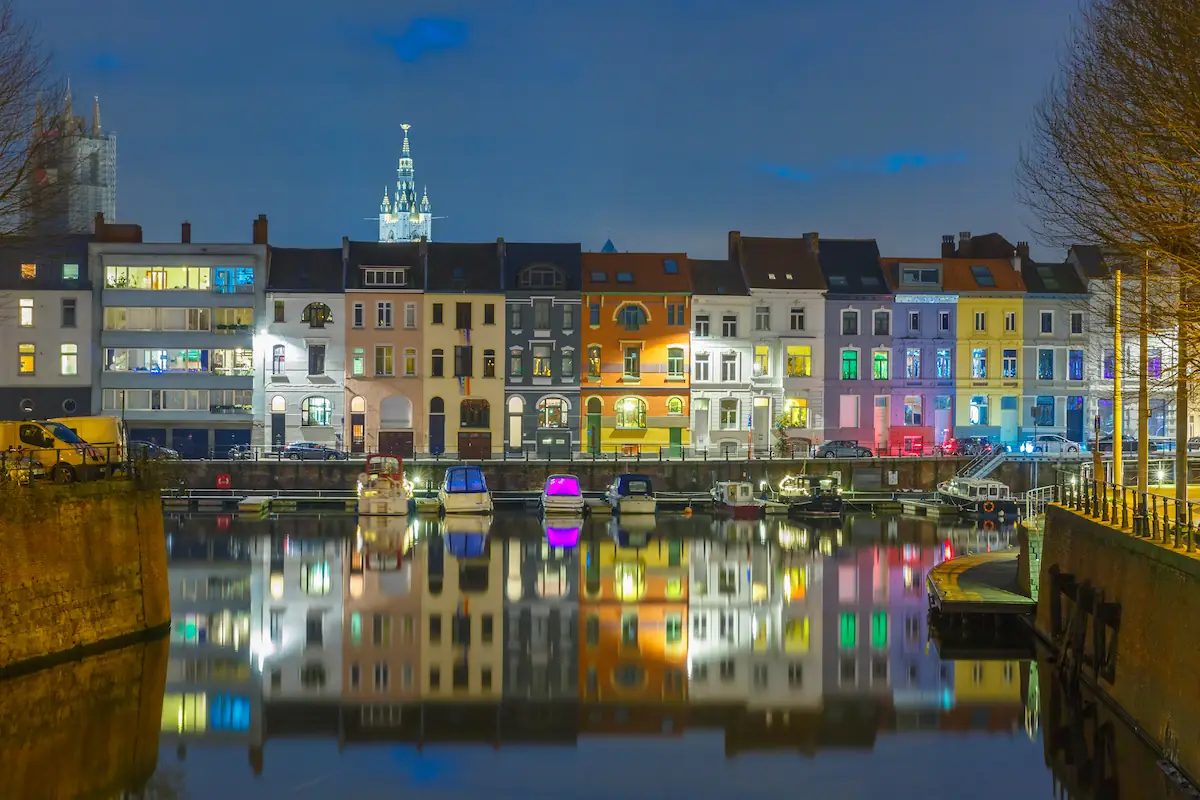 Een foto van enkele woningen aan het water in Gent, in de avond.