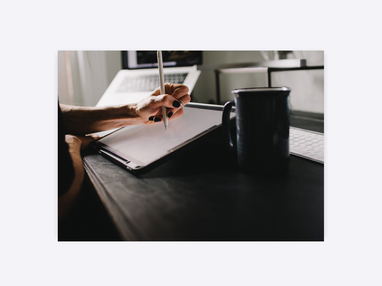 A person creating a design on an ipad, with a cup of coffee on their dark desk.