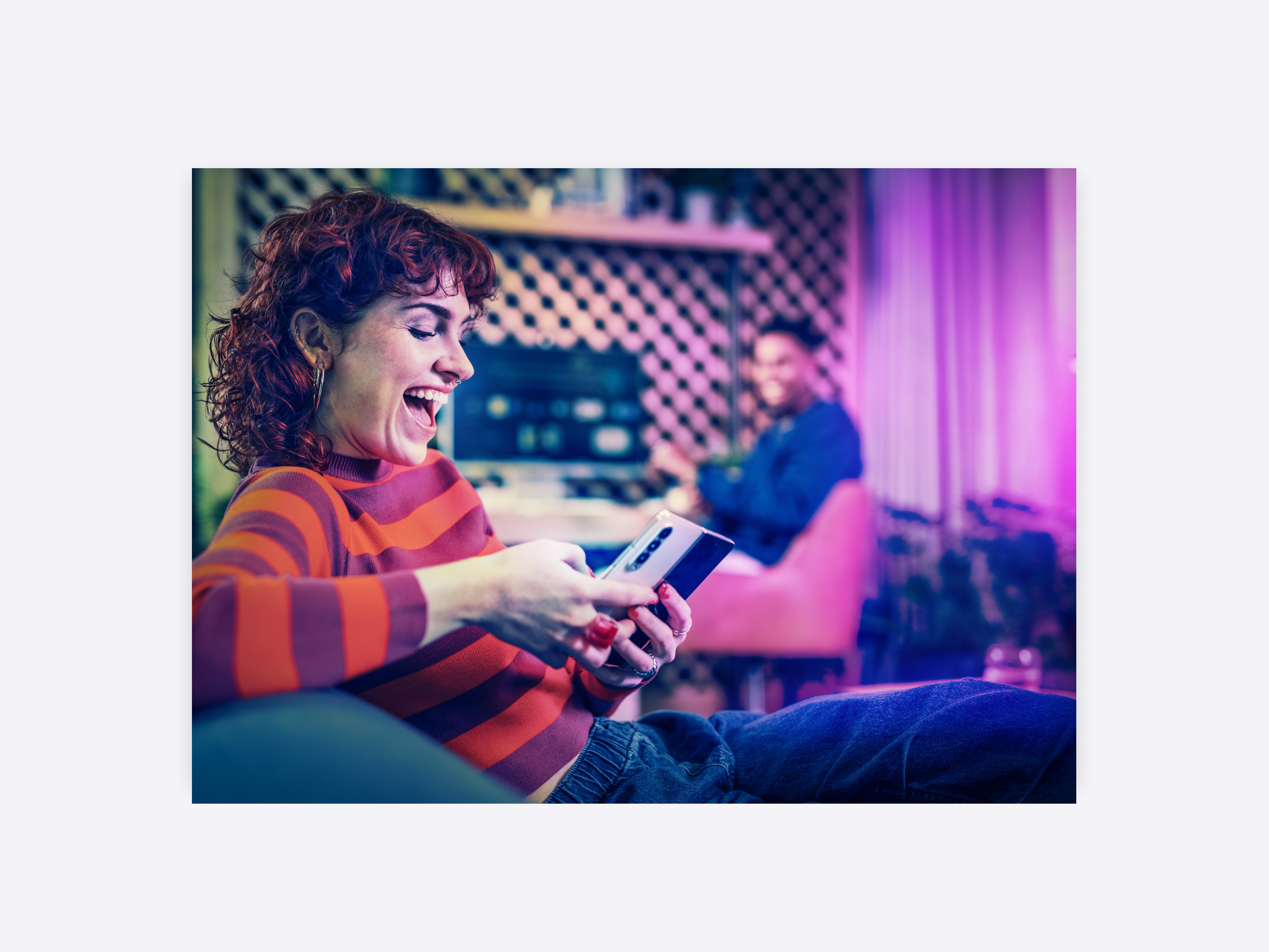 A young woman having a conversation with a friend while looking at her phone, laughing.