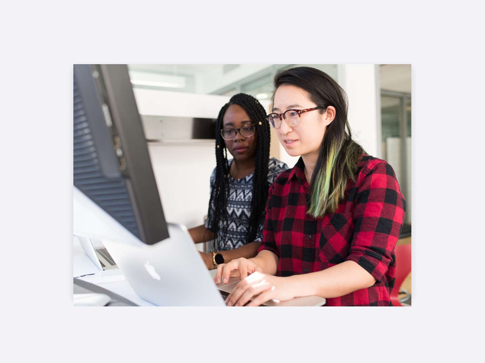 Photo of an art director mentoring their coworker. They are in the office, watching the screen. 