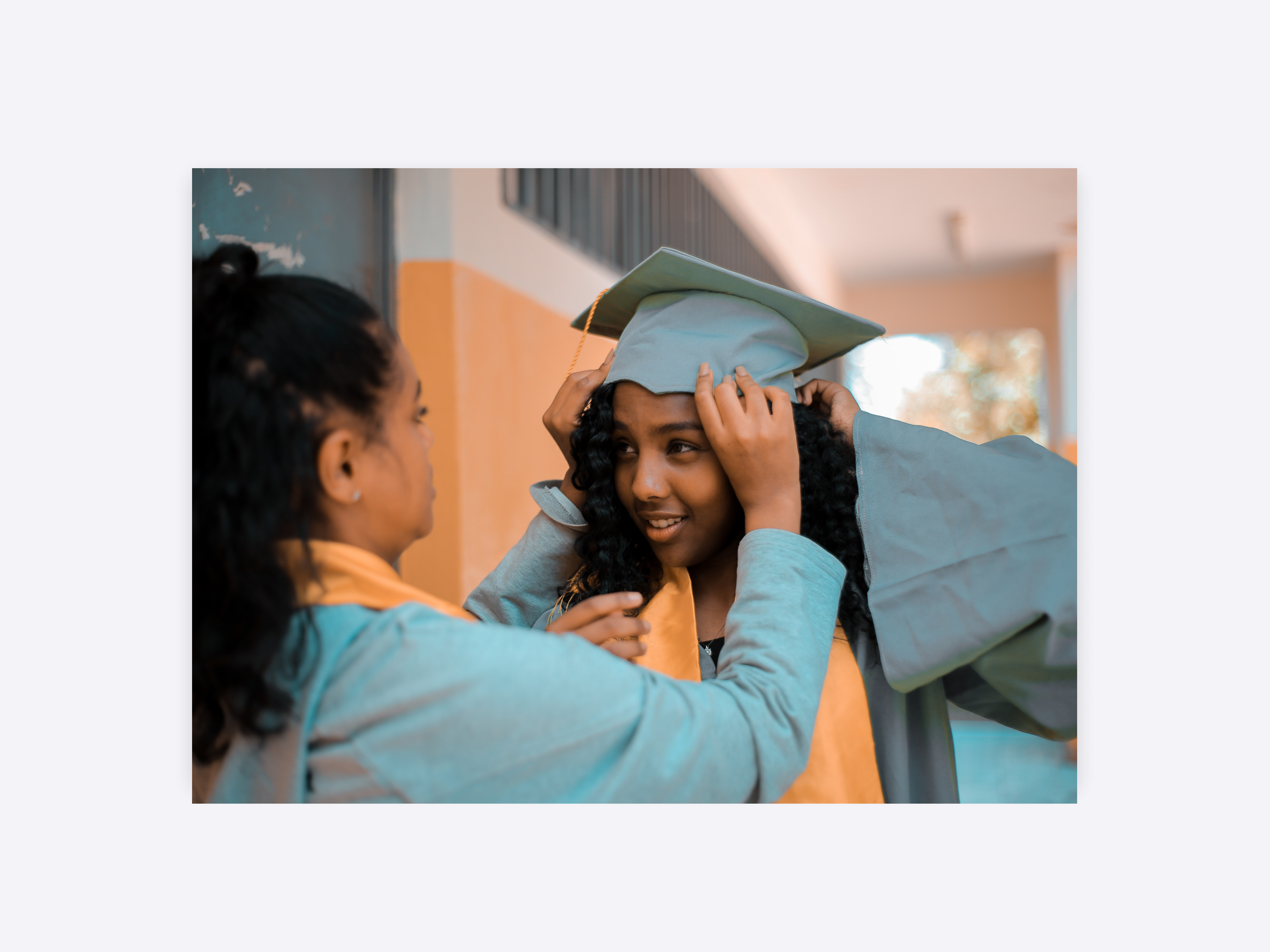 Two girls at graduation. One is helping the other with her graduation cap.