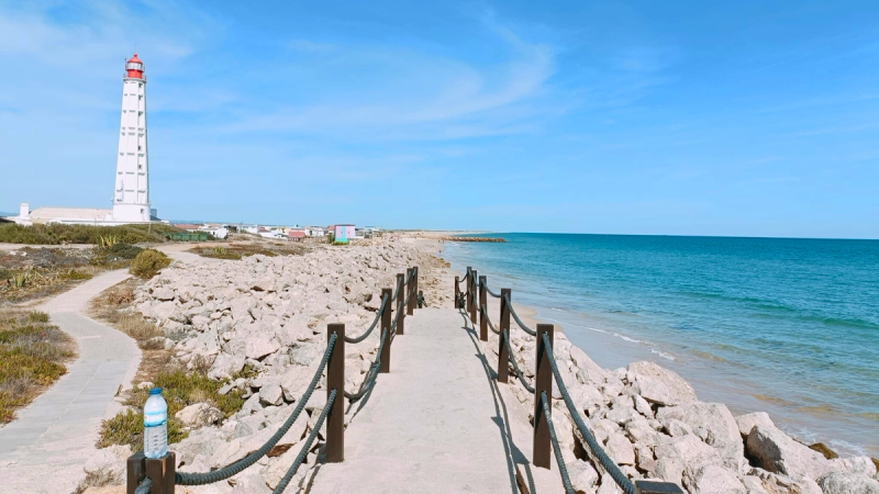 Walking path on Ilha do Farol in the Ria Formosa Natural Park, Algarve, Portugal, with the lighthouse and Atlantic coastline.