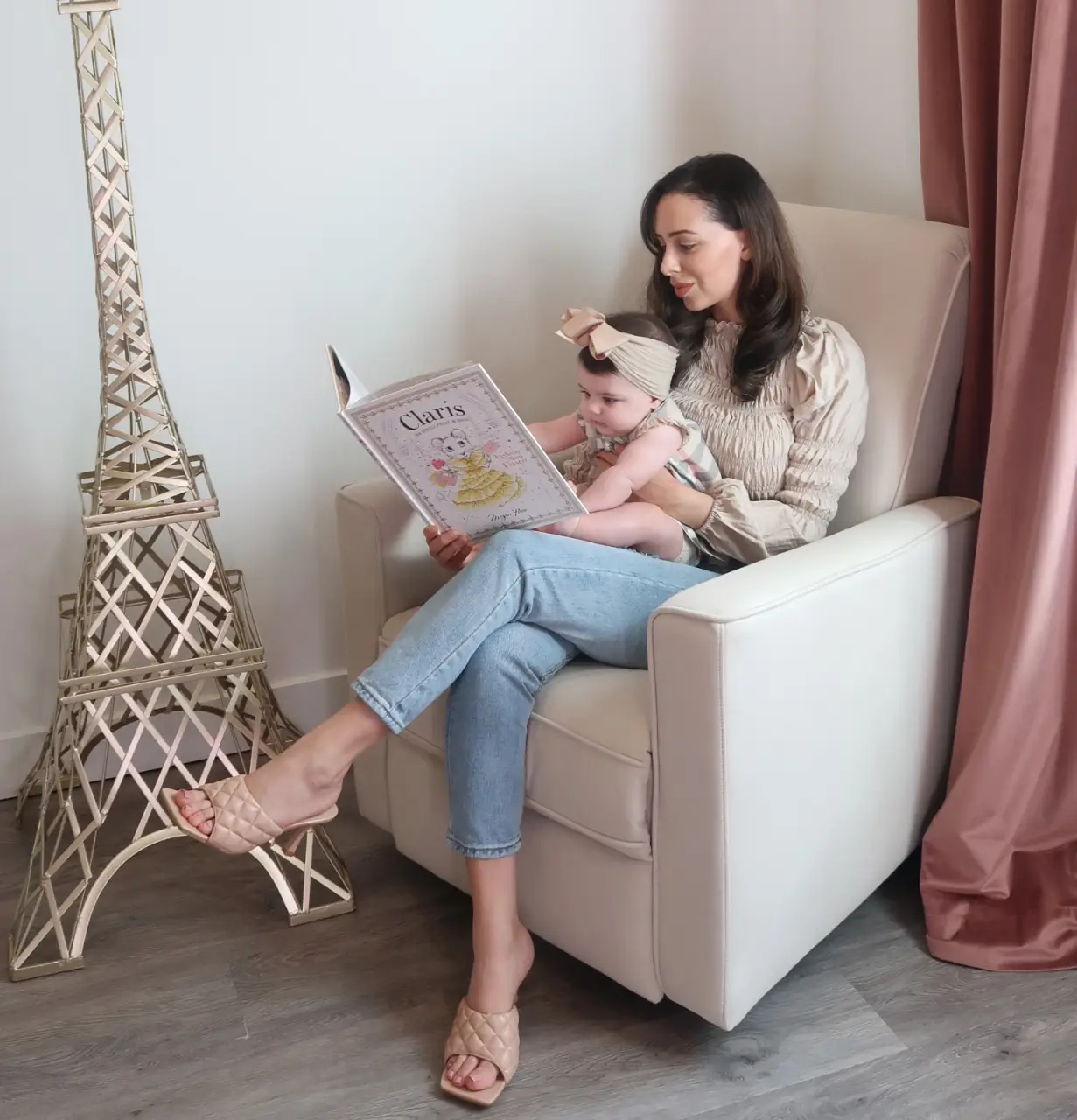 A mother sitting in Evolur Harlow Glider holding her baby while reading a children’s book