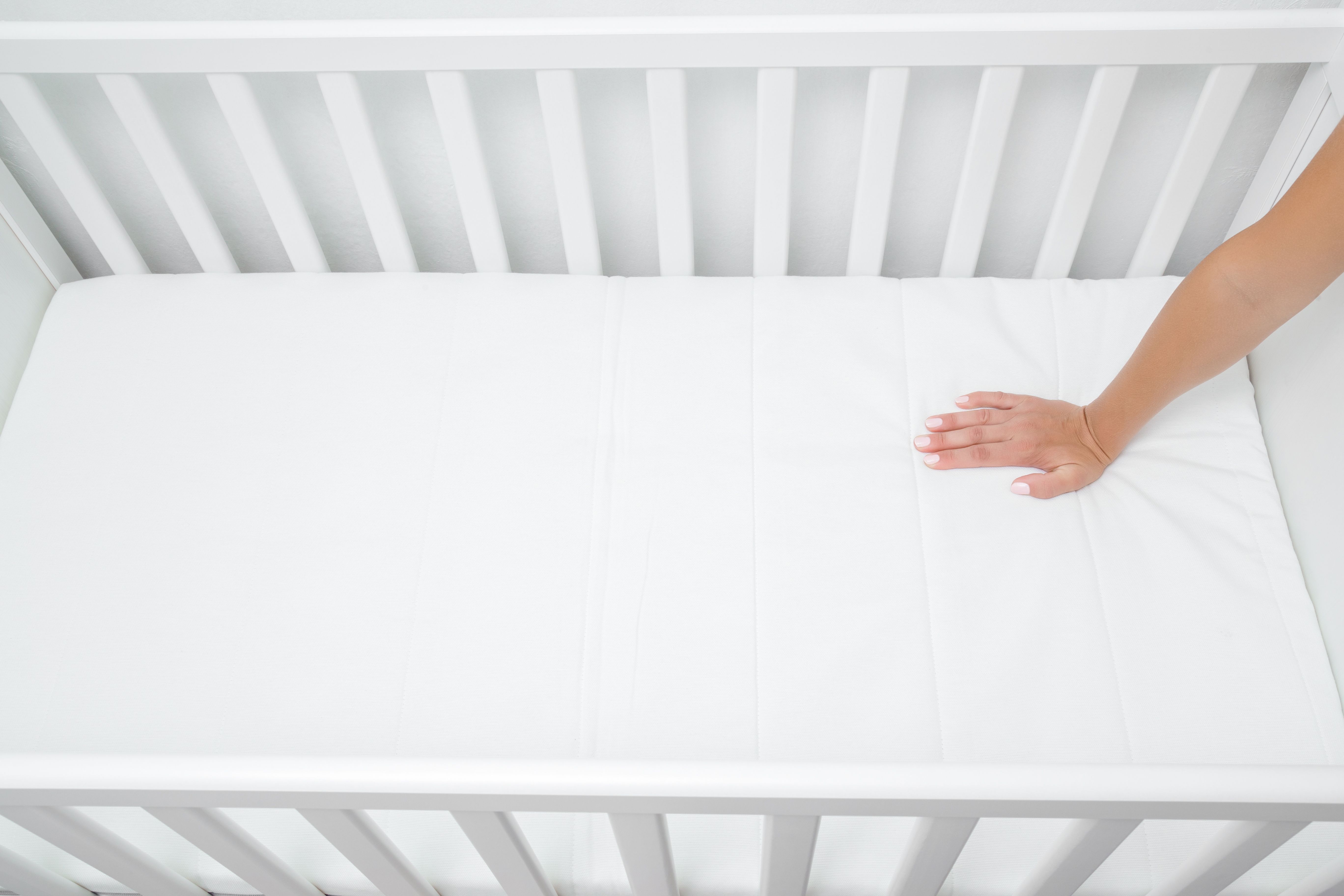 Hand press test on a firm white crib mattress inside a white baby crib