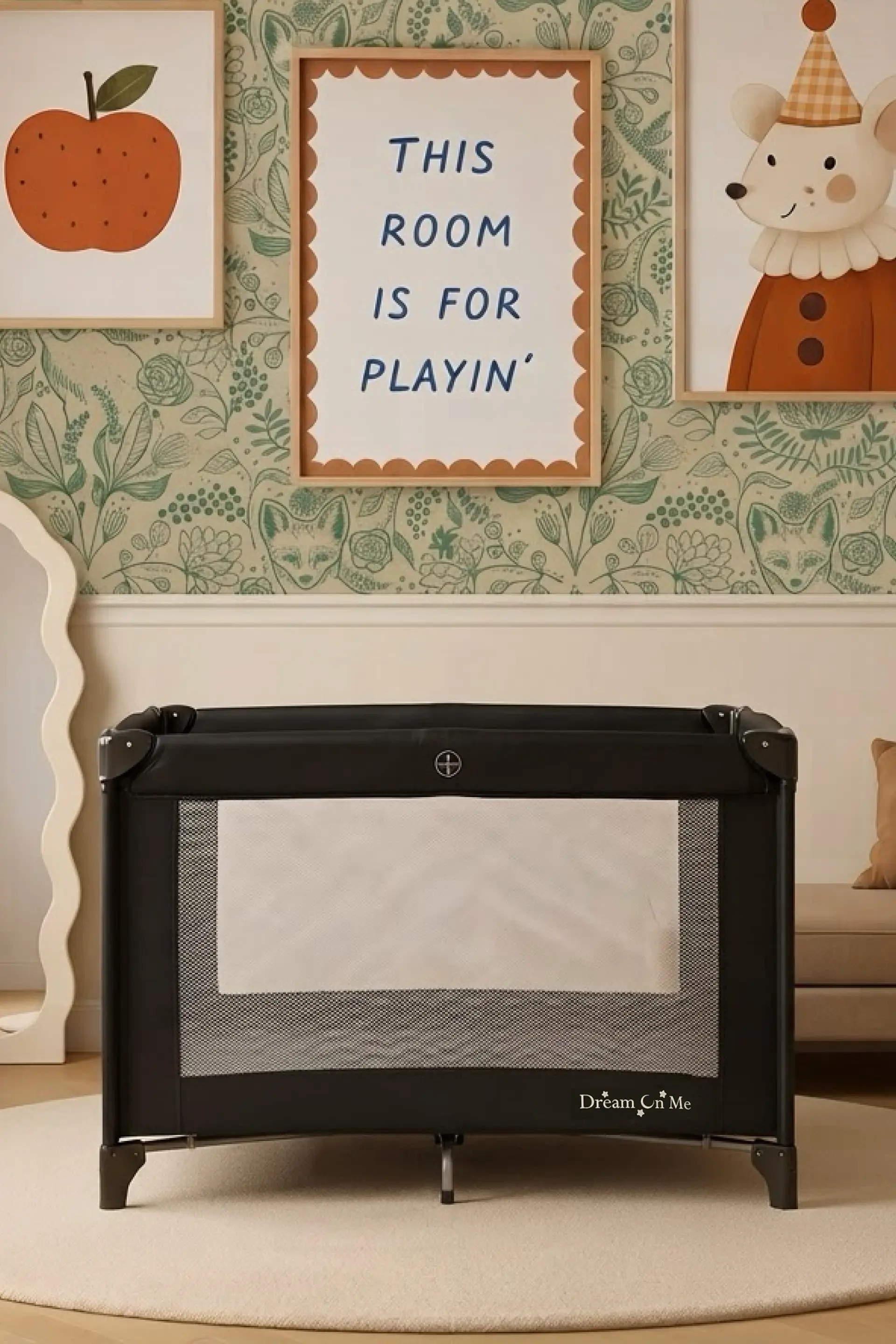 A black Dream On Me playard in a child's room with whimsical botanical and fox wallpaper and framed art, including a sign that reads "THIS ROOM IS FOR PLAYIN'".